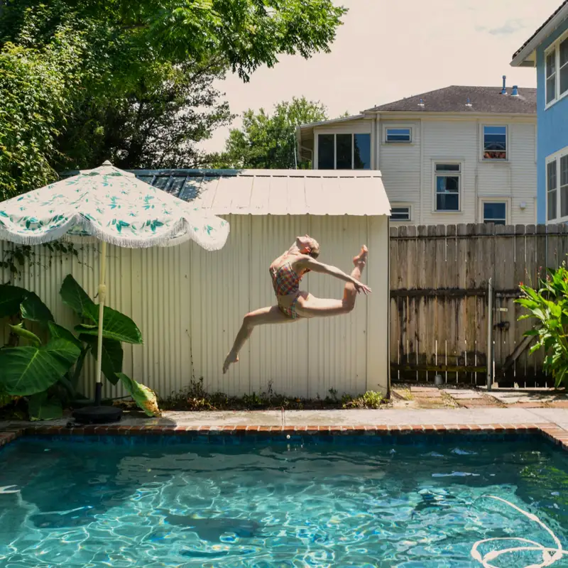 Email header photo: a person leaping through the air above a small backyard pool with a stone edge, a garden shed and an umbrella