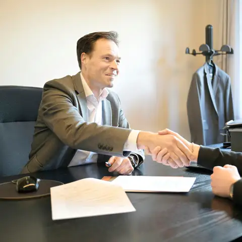 Two smiling men shaking hands across an office desk