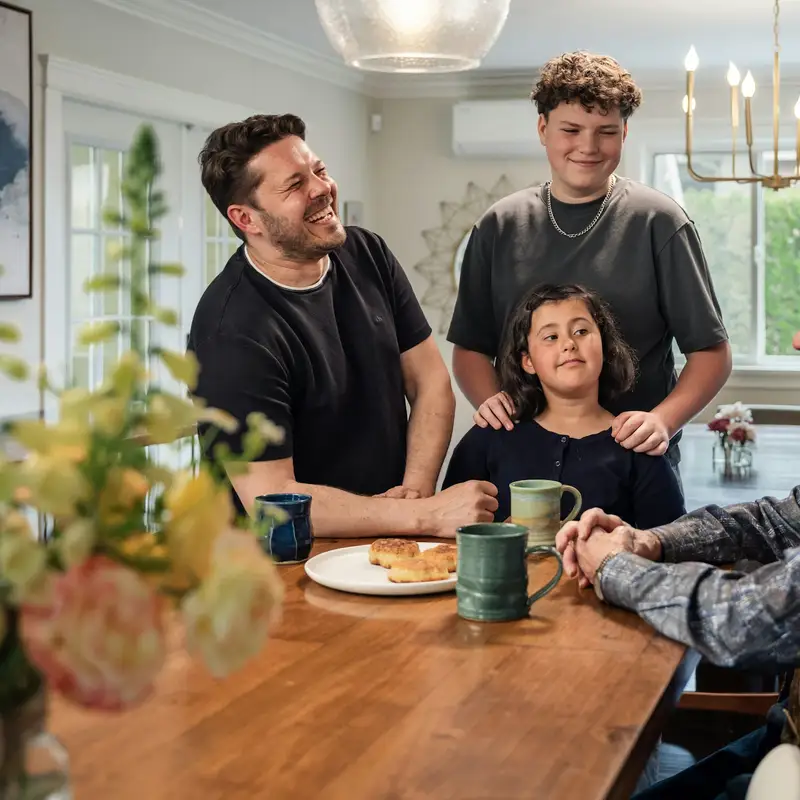 Email header photo: a father, a teenager and a young girl smiling around a wooden dining table with mugs and pastries, an older relative seated in the foreground