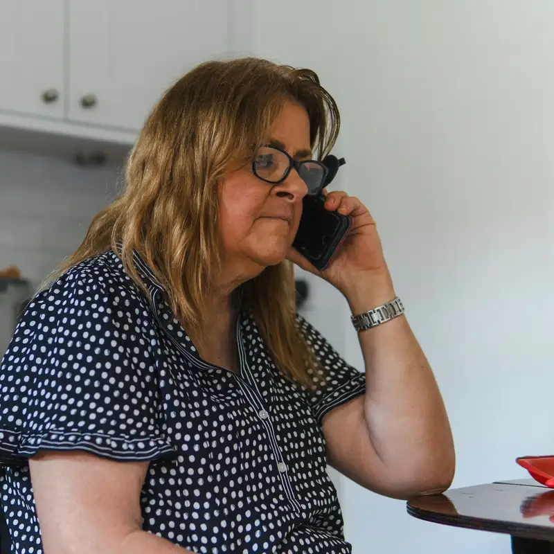 Email header photo: a woman in glasses making a phone call at her kitchen table