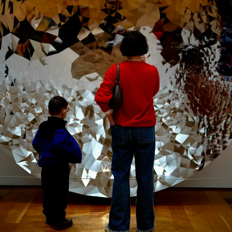 Email header photo: a woman in a red sweater and a young boy standing in front of a large round mirrored artwork in a museum gallery