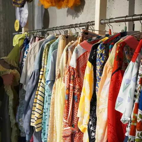 A woman looking through a rack of colorful secondhand blouses and shirts in a charity store