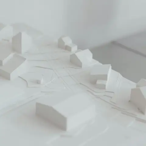 A white architectural site model showing low buildings, roads and lot lines on a sloped table