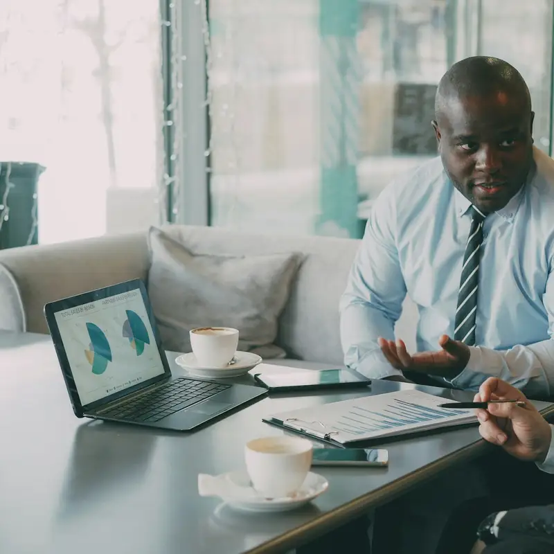 Email header photo: a man in a shirt and tie talking with a colleague over coffee, with pie charts on an open laptop and a printed report on the table