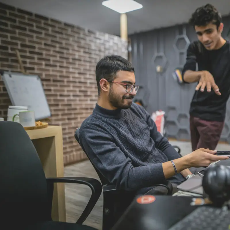 Email header photo: man standing beside a seated colleague at a computer desk, gesturing toward the screen
