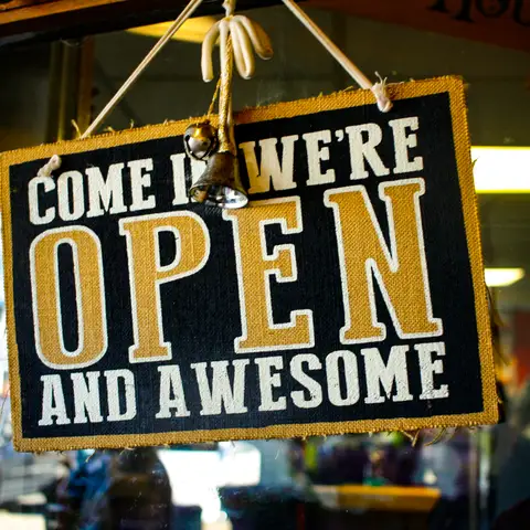 A navy and gold fabric sign reading come in, we are open and awesome hanging in a shop doorway