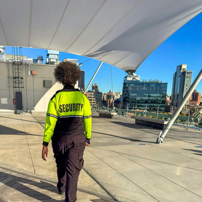 Email header photo: a security officer in a high-visibility jacket walks a rooftop terrace under a white canopy, with city towers and a blue sky ahead