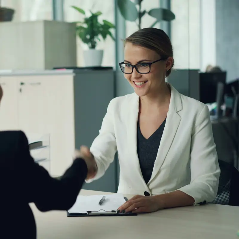 Email header photo: a smiling woman in glasses shaking hands across an office desk with a new candidate