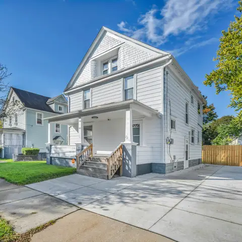 A white two-story house with a front porch, a new concrete driveway and a lawn on a sunny street