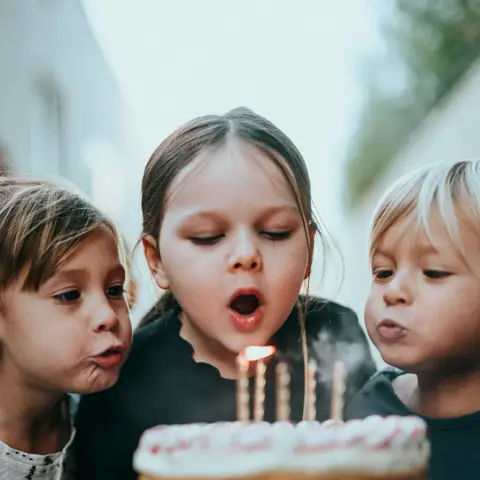 Three children blowing out the candles on a tall layered birthday cake