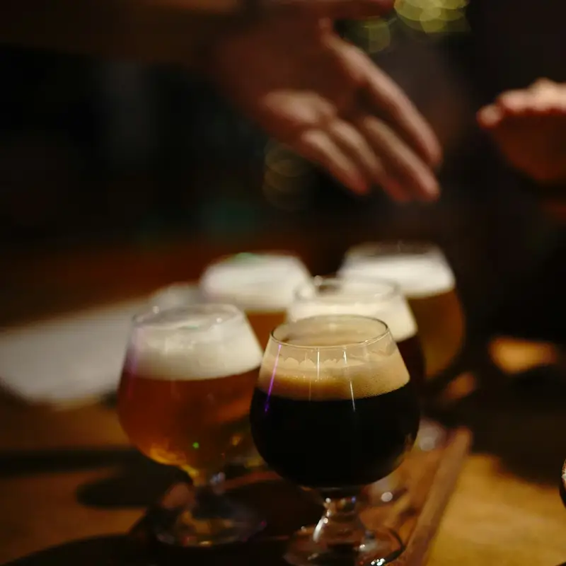 Email header photo: a tasting flight of four beers from pale gold to dark stout on a wooden paddle, with guests reaching across the table