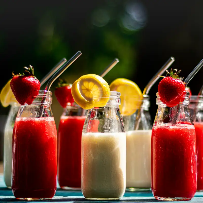 Email header photo: small glass bottles of strawberry and lemon drinks with metal straws, topped with fresh strawberries and lemon slices, on an outdoor table