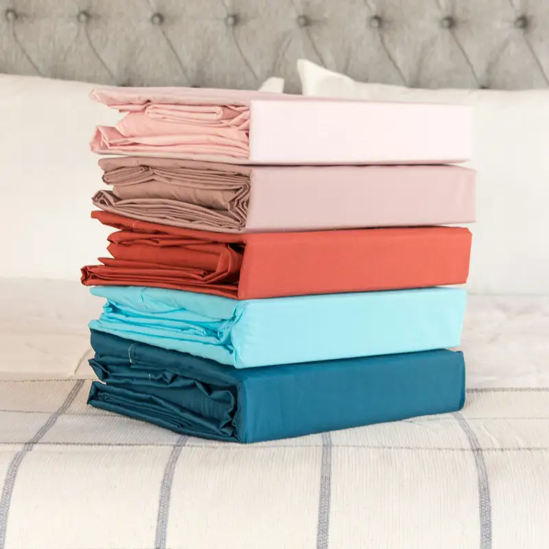Email header photo: a stack of folded sheet sets in pink, mauve, rust, sky blue and teal on a bed with a grey tufted headboard