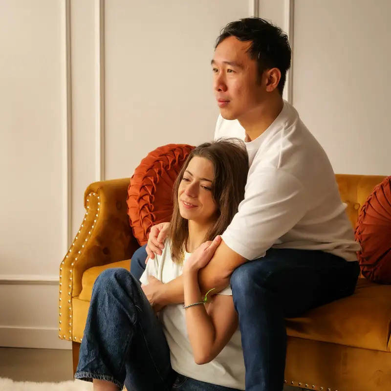Email header photo: a couple sitting close together on a mustard velvet sofa with round orange cushions at home
