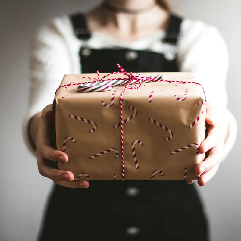 Email header photo: a person holding out a present wrapped in brown paper with a candy cane print and tied with red and white string