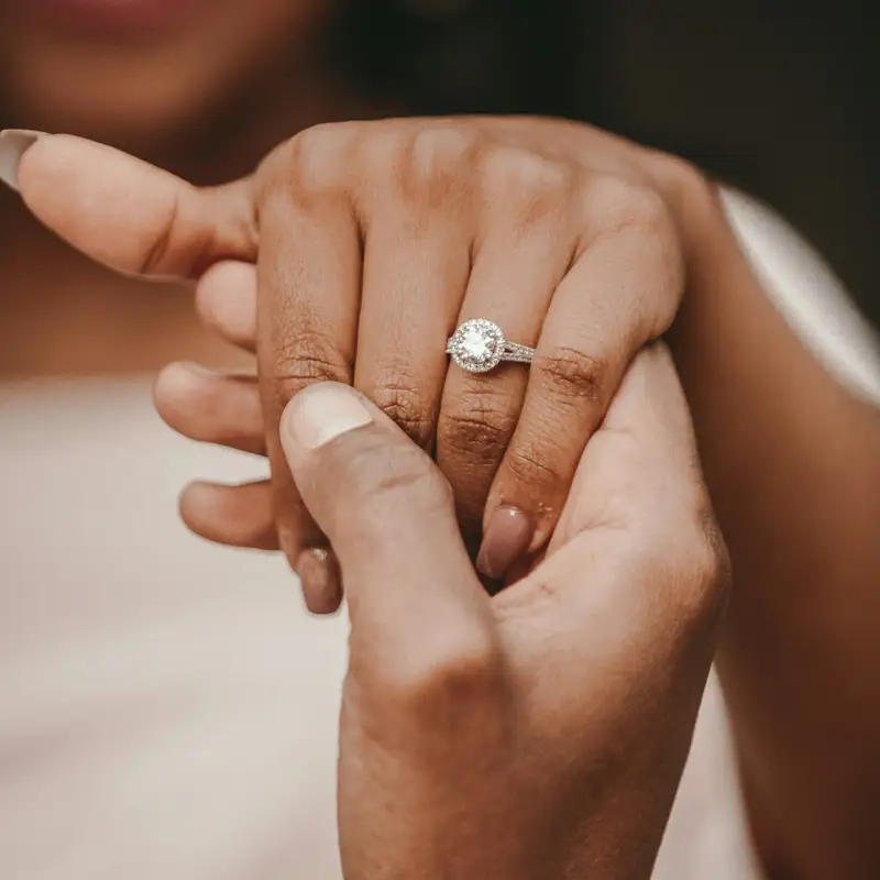 Email header photo: a man holding his partner’s hand, with a diamond solitaire engagement ring on her finger