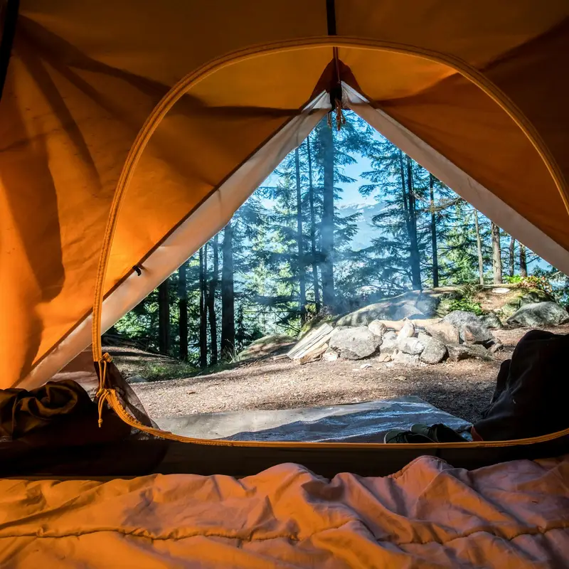 Email header photo: the view from inside an orange tent, with a sleeping bag in front and a stone fire ring among tall pines outside the open door