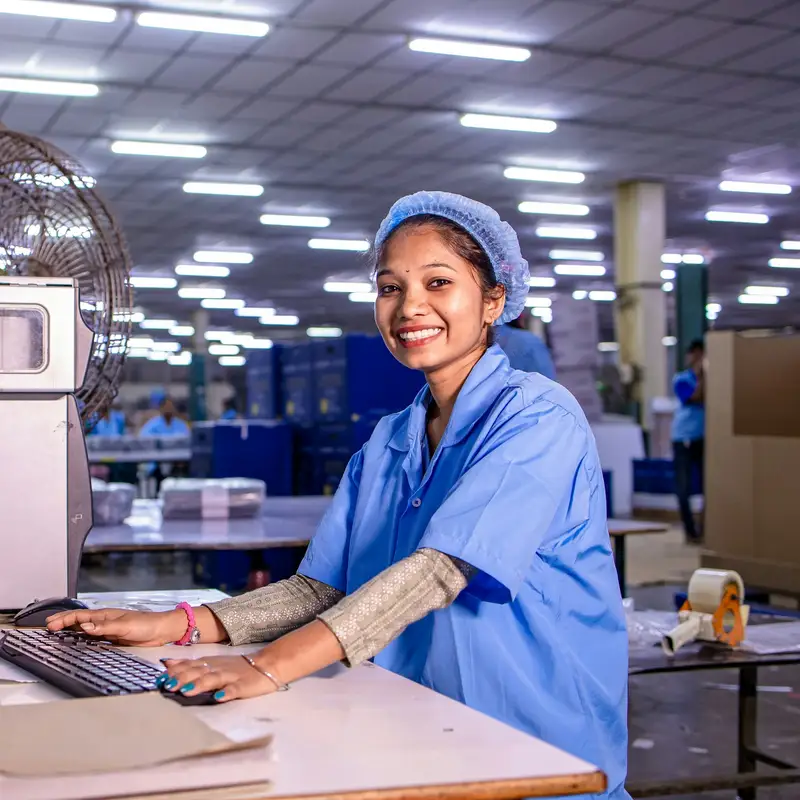 Email header photo: a smiling factory worker in a hairnet typing at a computer on the production floor