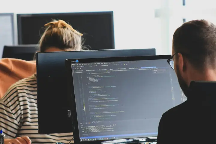 Two software developers writing code at monitors in a bright office