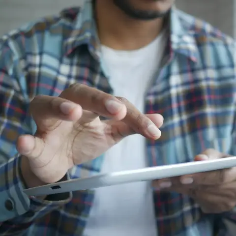 Person in a plaid shirt tapping through an app on a tablet