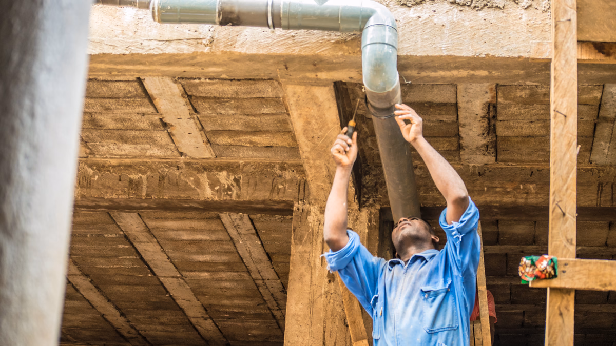 Licensed emergency plumber in work overalls installing copper piping overhead with professional tools