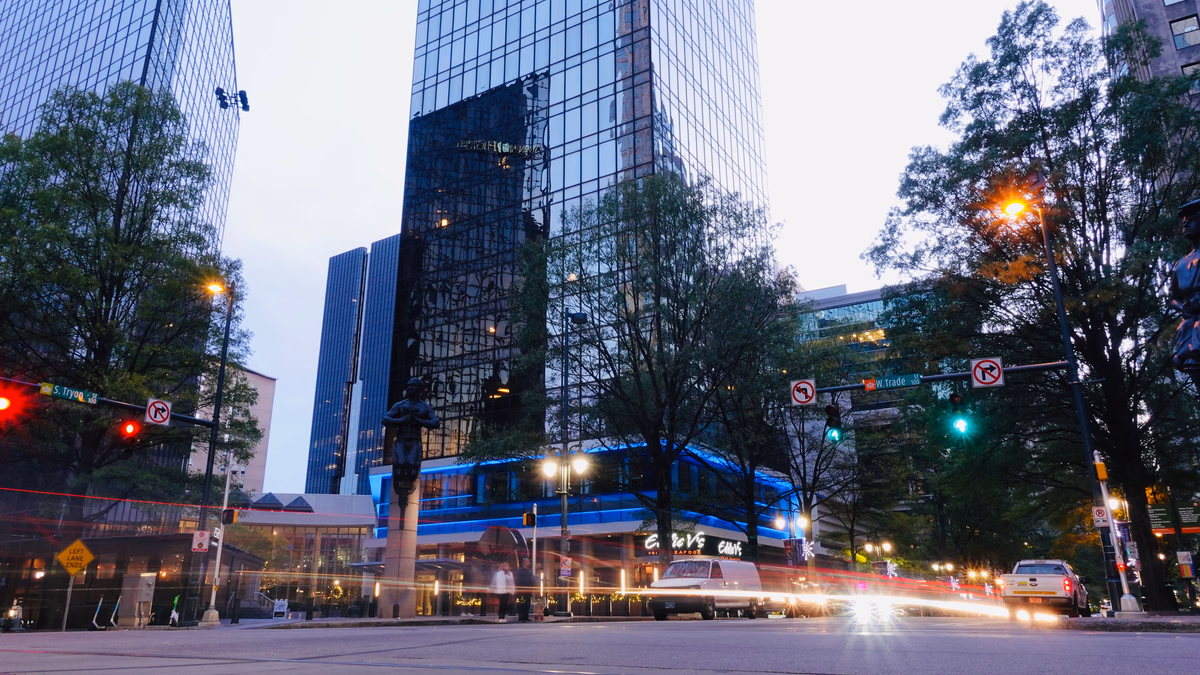 Evening street scene at the intersection of Trade and Tryon Streets in Uptown Charlotte North Carolina with illuminated corporate towers and pedestrians