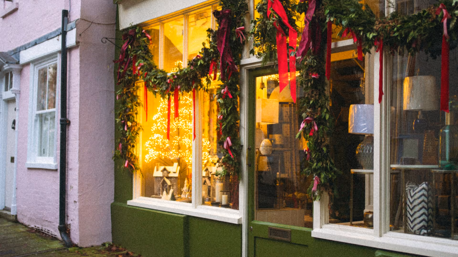 Independent shop window decorated with evergreen garlands, red ribbons and warm holiday lights