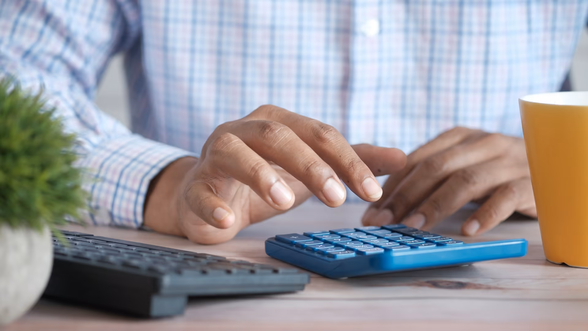Hands working out an advertising budget on a calculator at a desk beside a coffee mug