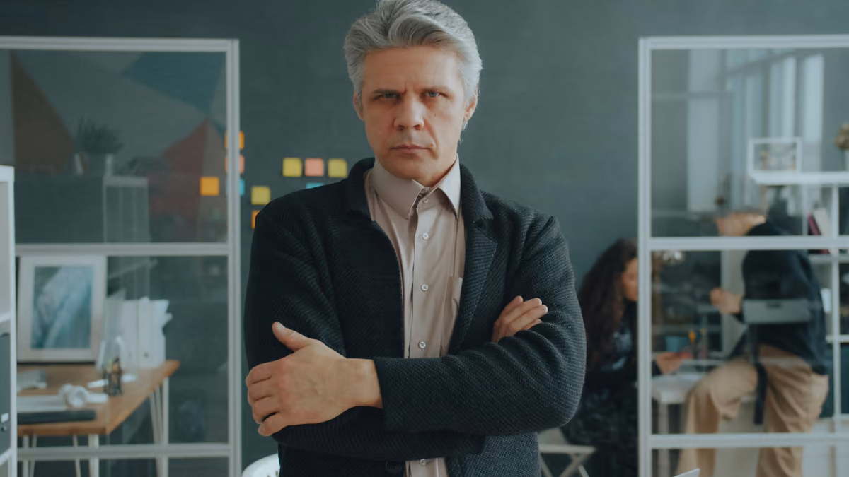 Senior business leader with grey hair standing with arms crossed in a bright modern office