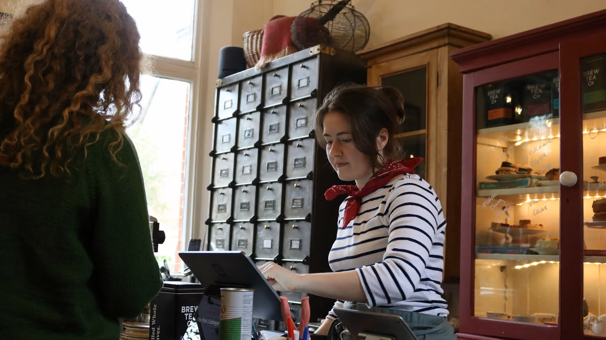 Shop owner in a red scarf ringing up a customer at the counter of a small independent store