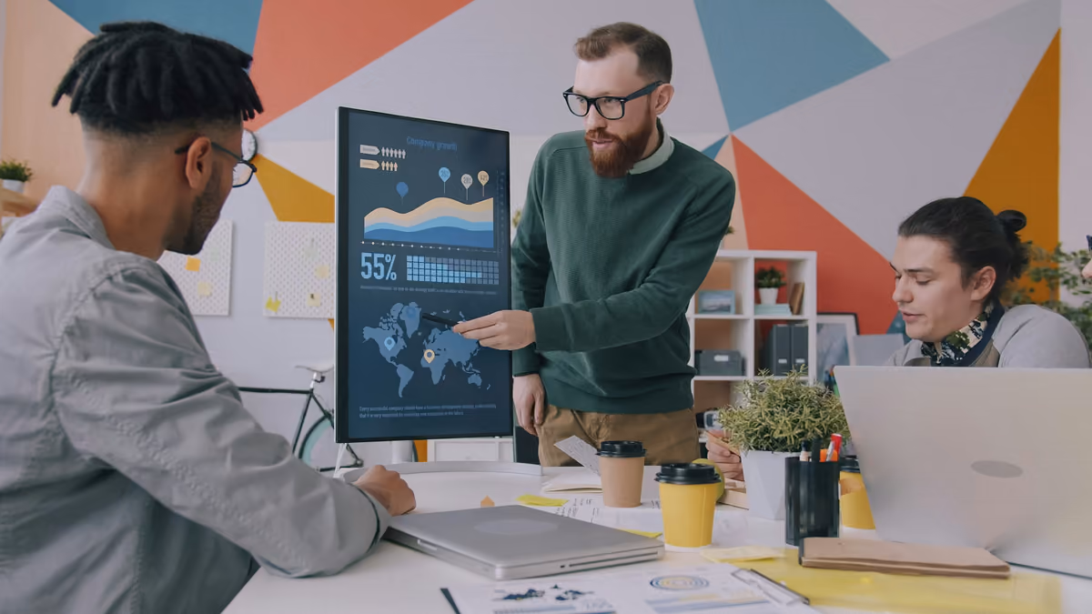 Manager pointing to a growth chart on a display while two colleagues review the numbers together