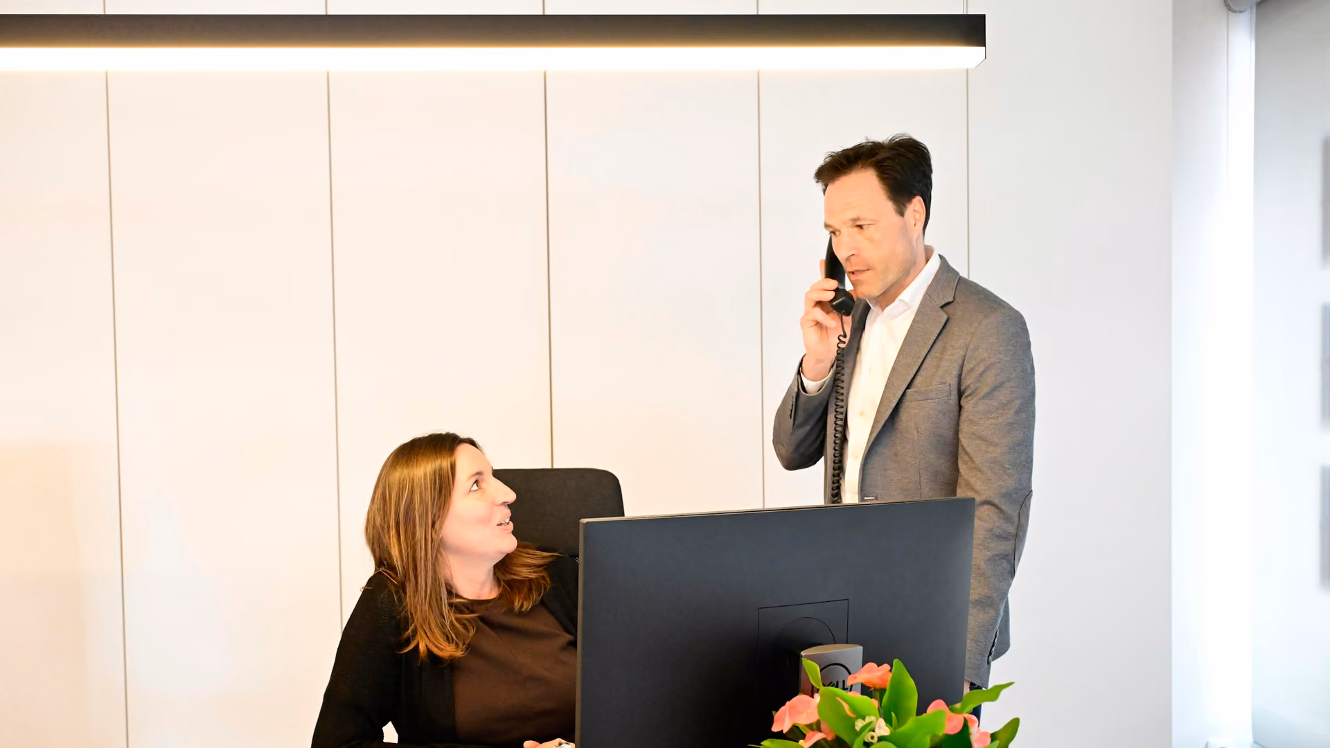 Business owner taking a customer call at the office while a colleague at her desk waits on the outcome