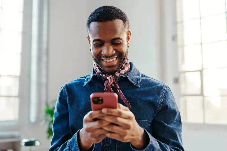 Smiling customer in a denim shirt reading a message on his phone