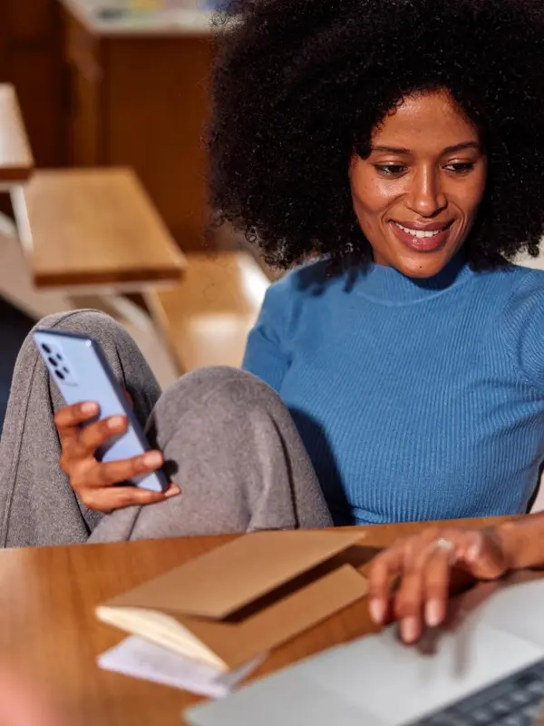 Business owner smiling at her phone while working on a laptop