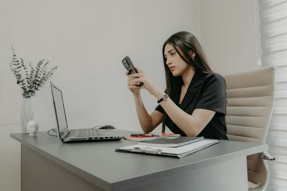 Sales rep at her desk calling a new lead on her phone with her laptop open