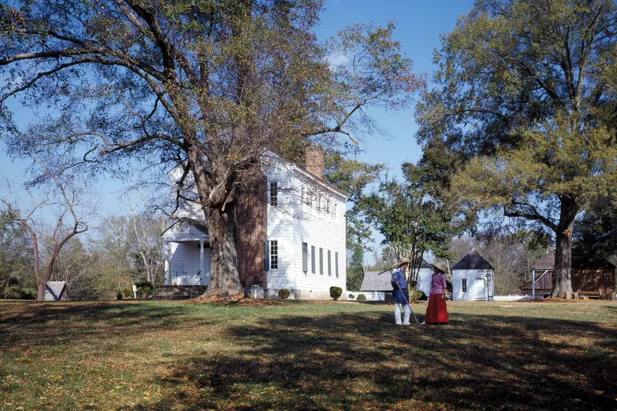 Latta Place farmhouse under old hardwoods with costumed interpreters on the lawn at Latta Nature Preserve, Huntersville