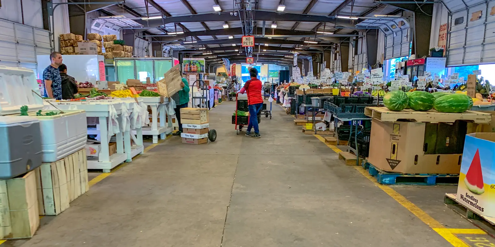 Open-air farmers market pavilion with shoppers browsing fresh regional produce and farm-fresh goods