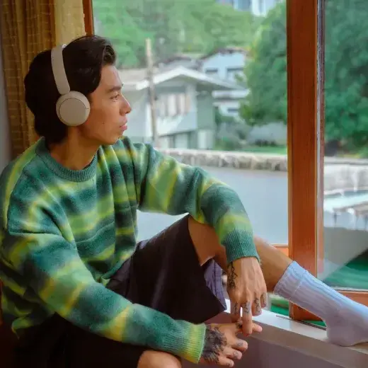 Young man with headphones relaxing by a window at home