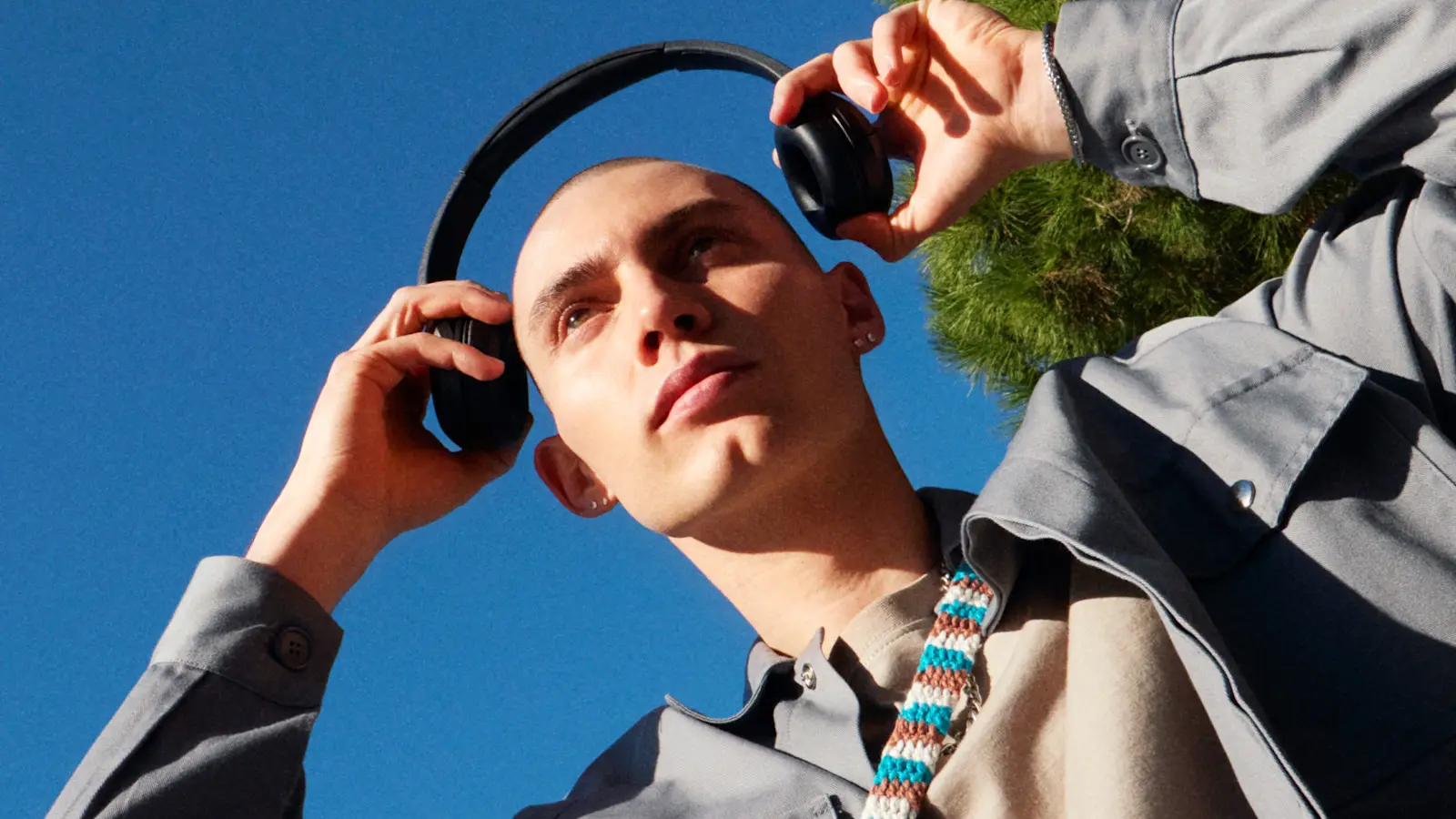 Young man putting on headphones under a blue sky
