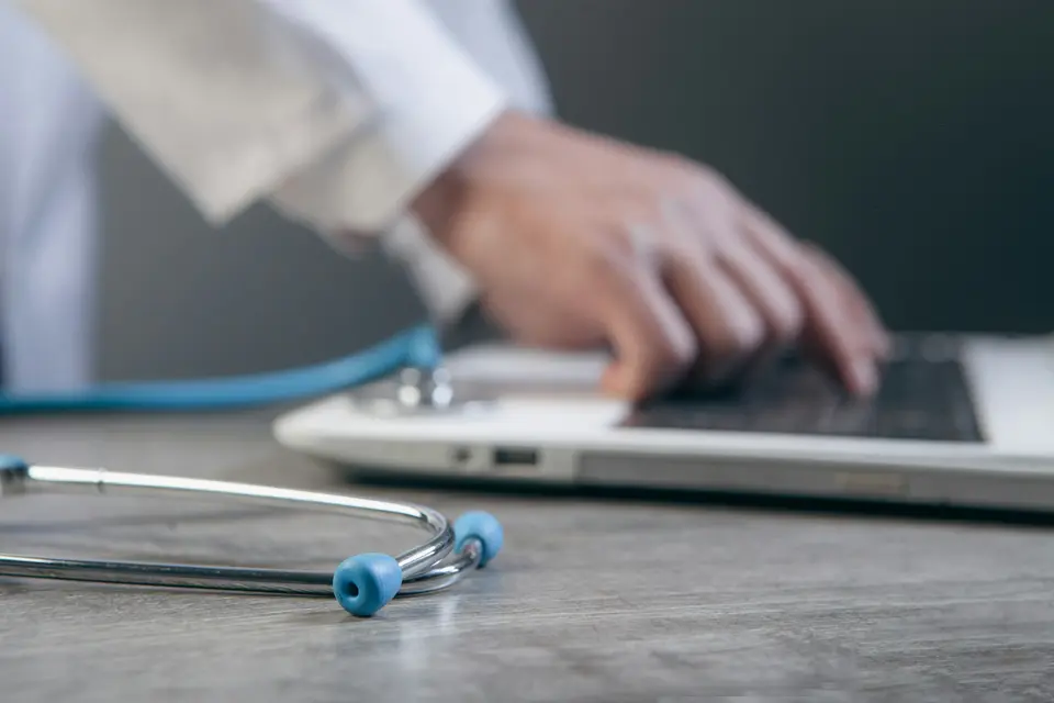 Doctor typing on a laptop with a stethoscope on the desk