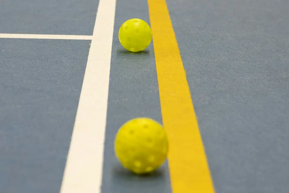 Two yellow pickleballs on a blue indoor court beside the lines