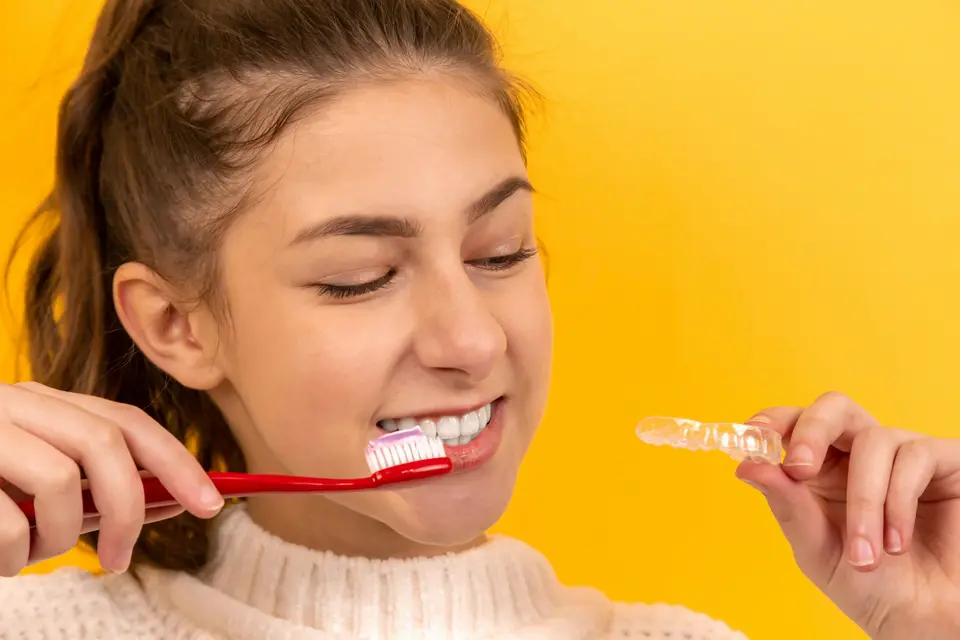 Smiling teenager brushing her teeth and holding a clear aligner