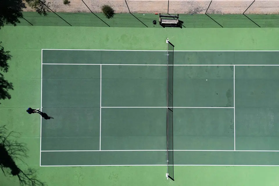 Two people playing tennis on a green court, seen from above