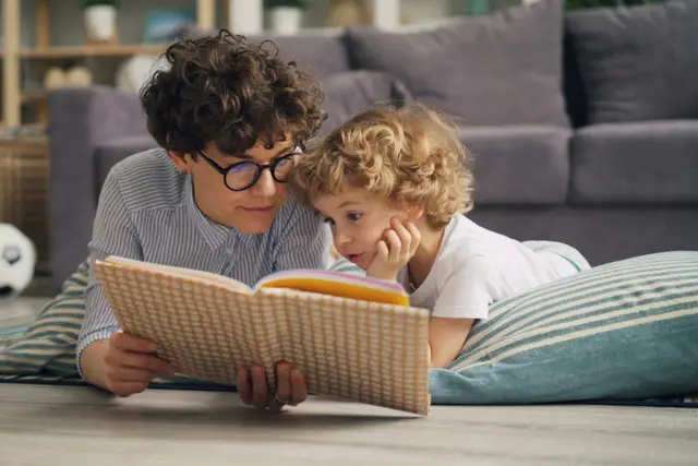 Mother and young child lying on the living room floor reading a book together