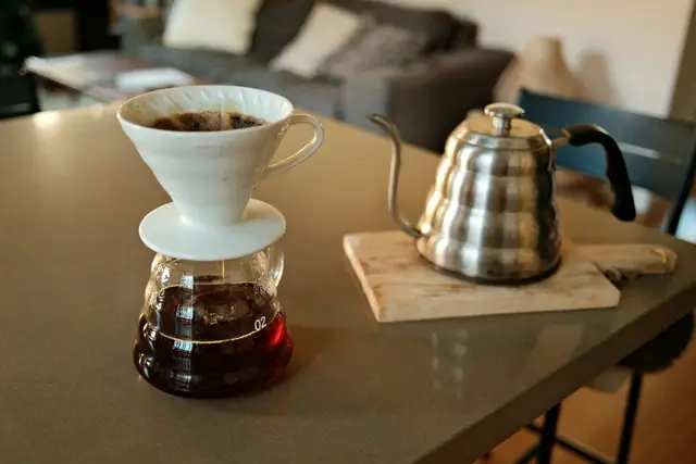 Pour-over coffee dripper on a glass carafe beside a steel kettle on a kitchen table