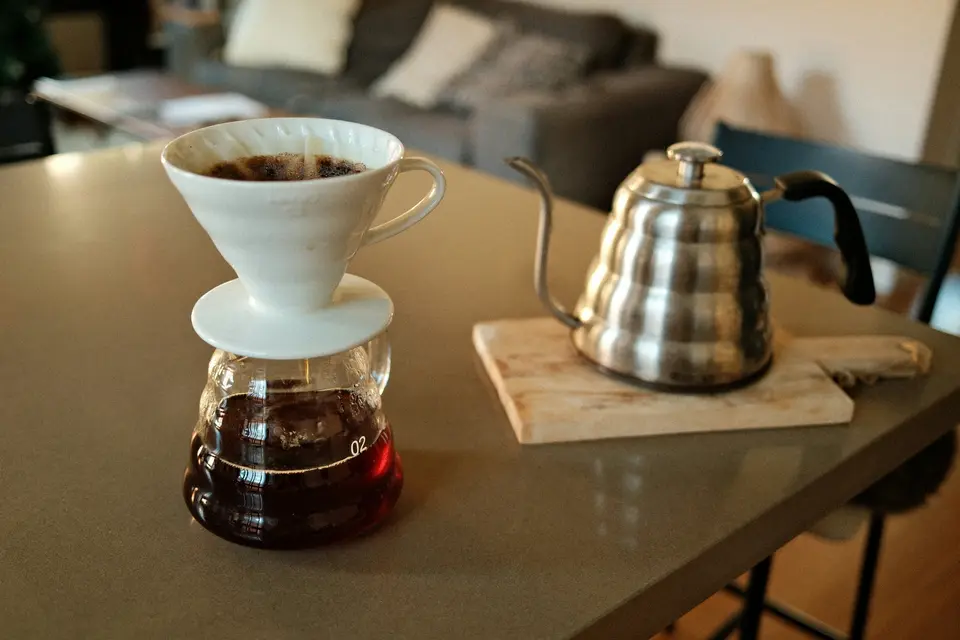 Pour-over coffee dripper on a glass carafe beside a steel kettle on a kitchen table