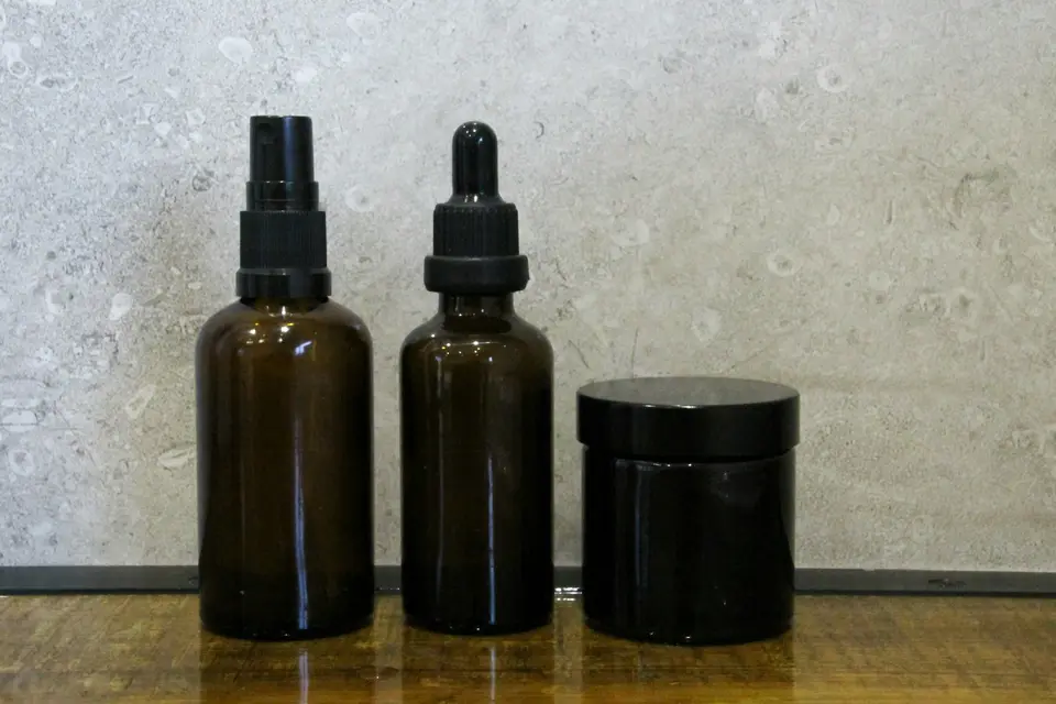 Two amber glass hair care bottles with a spray top and a dropper beside a jar on a stone shelf