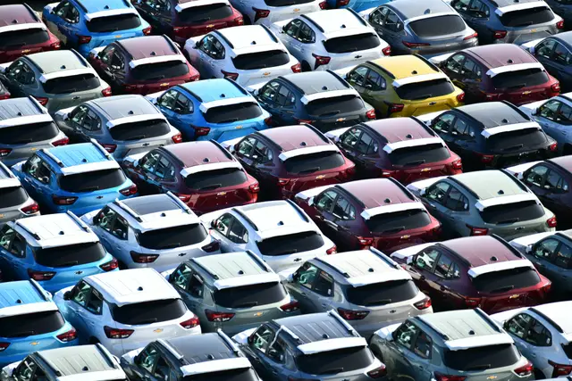 Rows of new cars in many colors parked on a large lot, seen from above