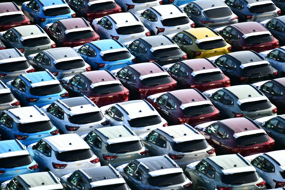 Rows of new cars in many colors parked on a large lot, seen from above