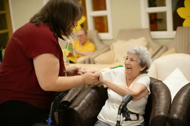 Caregiver holding hands with a smiling older woman in a bright living room
